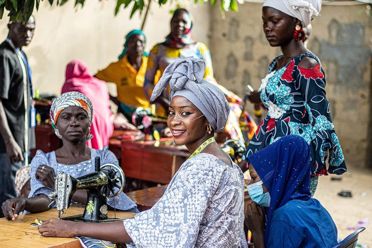 A smiling woman at a sewing machine in an outdoor tailoring workshop
