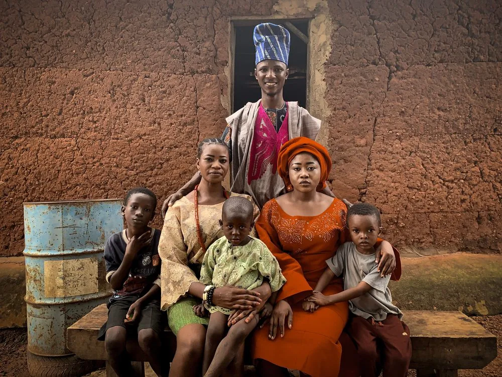 A family of women, men and young children sitting together outside a mud-brick home